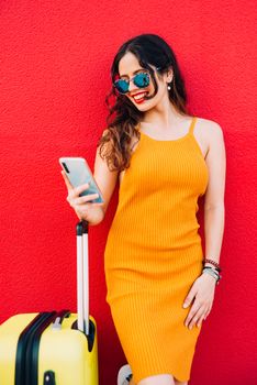 woman with a suitcase and smartphone waiting lean against a wall