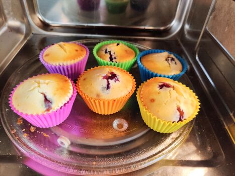 Freshly baked at home muffins in colorful cups placed in a shiny microwave. Shows the renewed interest in cooking due to the coronavirus pandemic lockdown