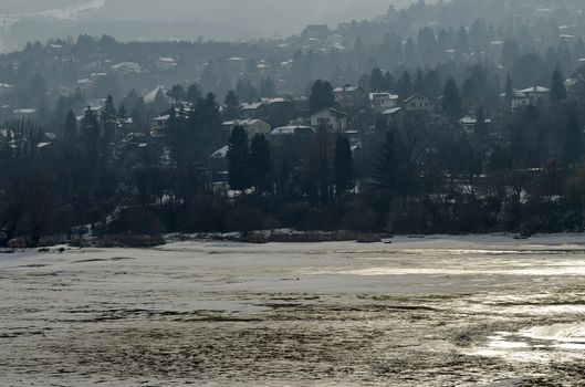 Winter scene with frozen lake, snowy mountain, glade, forest and residential district of bulgarian village Pancharevo, Sofia, Bulgaria