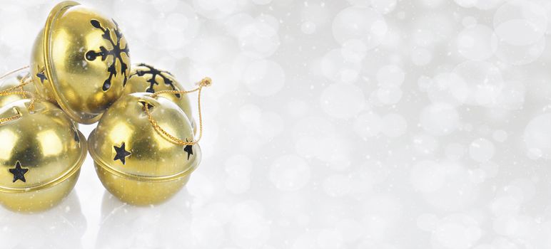 Christmas Concept: Gold Jingle bells on a snowy bokeh silver background with copy space.