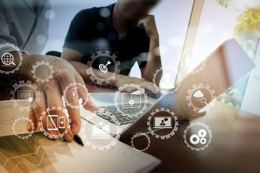 E-learning with connected gear cogs connected diagram virtual dashboard.business documents on office table with smart phone and laptop and two colleagues discussing data in the background.