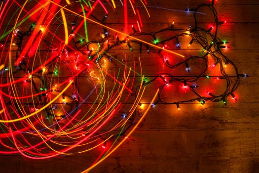 Colorful Christmas garland warm lights. Multicolored light lines. Wooden background. Long exposure. Top view. Horizontal shot. Copy space.