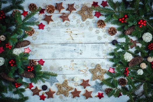 Christmas background. Frame made with fir twigs, red berries, cones and Xmas decoration on a wooden board in vintage style. Flat lay, top view, copy space. 