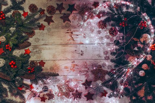Christmas background with fir twigs, red berries, cones and Xmas decoration, lights on a wooden board in vintage style. Flat lay, top view.