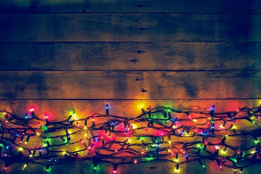 Colorful Christmas garland warm lights. Multicolored lights. Wooden background. Long exposure. Top view. Horizontal shot. Copy space.