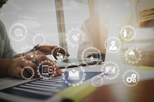 E-learning with connected gear cogs connected diagram virtual dashboard.business documents on office table with laptop computer and graph business diagram and man working in the background