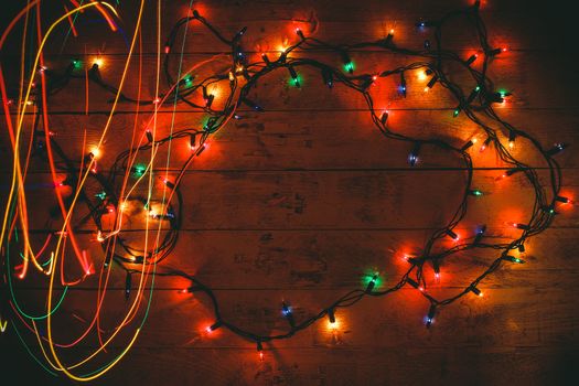 Colorful Christmas garland warm lights. Multicolored light lines. Wooden background. Long exposure. Top view. Horizontal shot. Copy space.