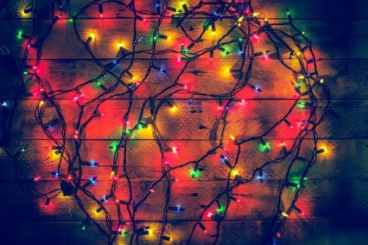Glowing colorful Christmas lights on a wooden background. Christmas decor. Garland. New Year. Flat lay, top view, copy space. 