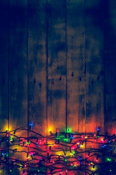 Colorful Christmas garland warm lights. Multicolored lights. Wooden background. Long exposure. Top view. Vertical shot. Copy space.