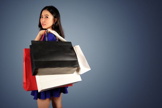 Happy women in blue dress with a shopping bag on dark blue background and clipping path with space for text