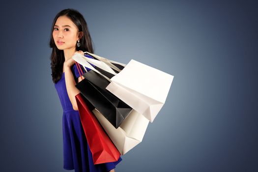Happy women in blue dress with a shopping bag on dark blue background and clipping path