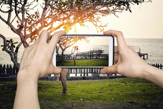 Girl taking pictures on mobile smart phone Happy couple relaxing in a tree by the sea