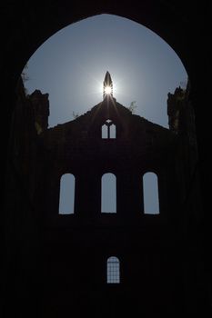 Plants grow atop the stone walls of this ruined cathedral, and sun flare enhances religious feeling of this ruined cathedral. Old windows silhouetted
