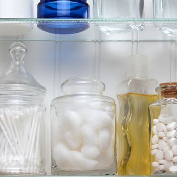 Closeup of two shelves of a medicine cabinet. A bottle of tablets, cotton balls and cotton swabs and assorted jars and bottles of soap and lotions. Square format.