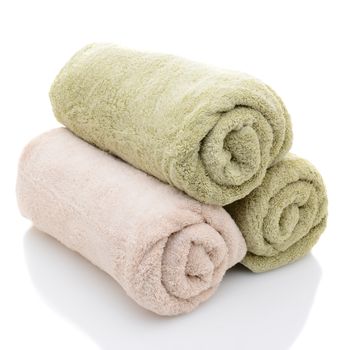 Three rolled bath towels freshly laundered on a white background with reflection. Closeup looking at the towel ends.