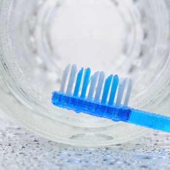 A blue toothbrush laying on a wet bathroom counter with a glass on its side in the background.