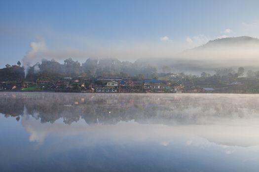 Mountain view and village under cloudy sky and mountain reflect on water in dam at day time