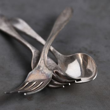 Closeup still life of antique forks and spoon on gray metal background,. Shallow depth of field. 
Square format.
