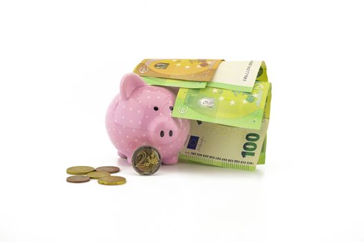 Euro banknotes and loose coins with a little ceramic pink piggy bank over a white background with copyspace for savings, finances or money related themes