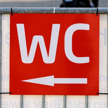 Red sign on the outdoor area at a festival with the white written sign "WC" and an arrow pointing towards the toilet, germany