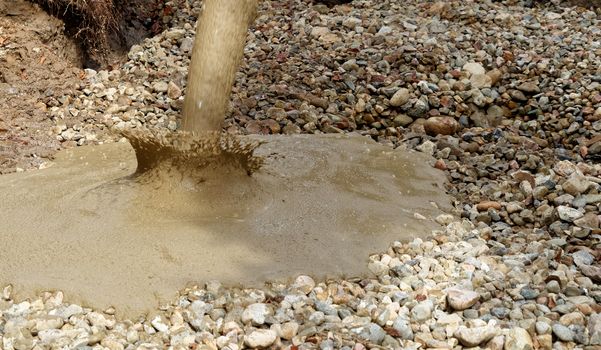 Liquid soil is poured from the concrete mixer onto the floor of the excavation pit covered with coarse gravel and stones, Germany