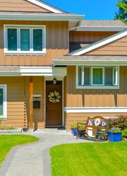 Entrance of residential house in perfect neighbourhood. Family house with big green lawn and trees in front on blue sky background