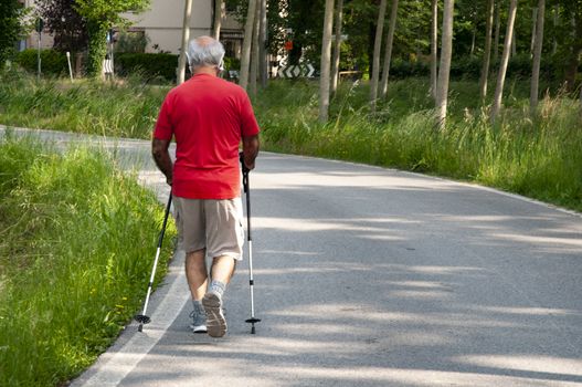 Old man walking with sticks on path walk in the sunset light