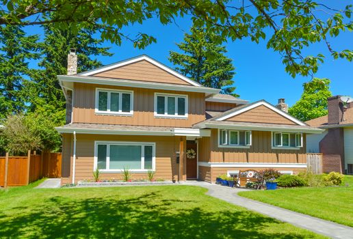 Average residential house in perfect neighbourhood. Family house with big green lawn and trees in front on blue sky background