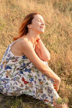 Tender beautiful red-haired girl enjoys the sunset in a field with a hill