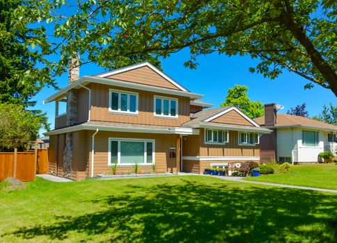 Average residential house in perfect neighbourhood. Family house with big green lawn and trees in front on blue sky background