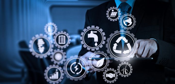 Sustainable development with icons of renewable energy and natural resources preservation with environment protection inside connected gears.Businessman hand working with a digital tablet on meeting room background