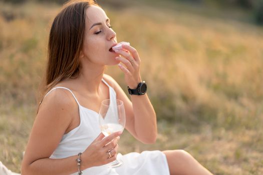 Gorgeous young brunette girl in a white sundress enjoying a picnic in a picturesque place. Romantic picnic.