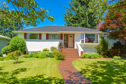 Average residential house in perfect neighbourhood. Family house with big yard and green lawn in front on blue sky background