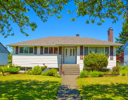 Average residential house in perfect neighbourhood. Family house with big yard and green lawn in front on blue sky background