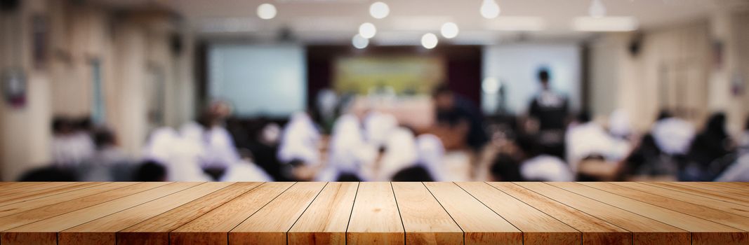 Panoramic empty clean wood counter table top on blur student study in classroom white light background for product education learning hall centre, Abstract Blurry wooden desk scene display or montage.