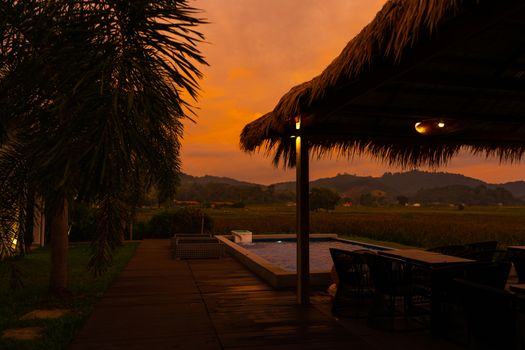 Beautiful orange fiery sunset in the tropics. Street canopy from hay, next to the pool and overlooking the rice field