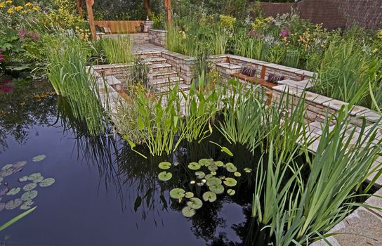 A colourful garden with water features a summer house and exotic plants and flowers