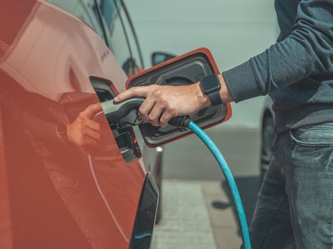 The man charges the electric car at the charging station.