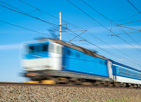 Blue train powered by electricity, drives through the countryside.