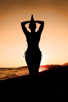 Woman doing yoga at sunset on the beach