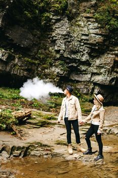 Young and beautiful couple at the mountain waterfall - Happy tourists visiting mountains. Lovestory. Tourists in hats. Military fashion