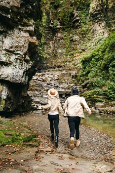 Young and beautiful couple at the mountain waterfall - Happy tourists visiting mountains. Lovestory. Tourists in hats. Military fashion