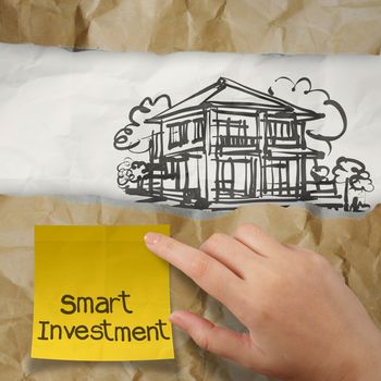 hand holding smart investment sticky note with  house on wrinkled paper as concept