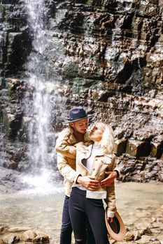 Young and beautiful couple at the mountain waterfall - Happy tourists visiting mountains. Lovestory. Tourists in hats. Military fashion