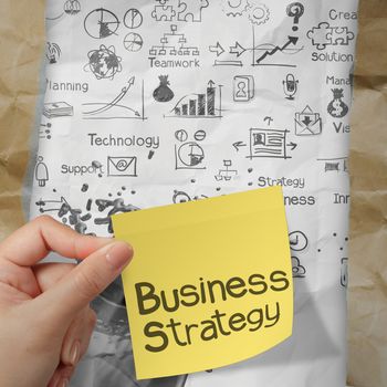 hand holding  business strategy on crumpled paper background and sticky note as concept