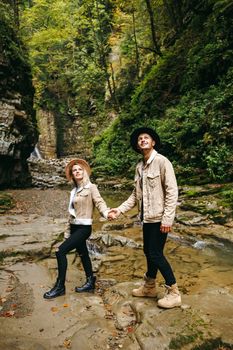 Young and beautiful couple at the mountain waterfall - Happy tourists visiting mountains. Lovestory. Tourists in hats. Military fashion