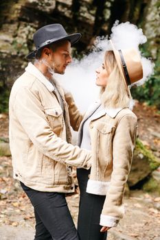 Couple in vape cloud. Two in smoke. Tourists in cold autumn forest with vape. Man and women in smoke. Two smokers. Beautiful couple in fog. E-cigarettes and people