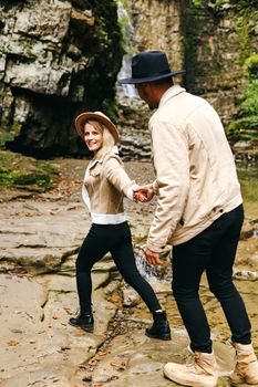 Young and beautiful couple at the mountain waterfall - Happy tourists visiting mountains. Lovestory. Tourists in hats. Military fashion