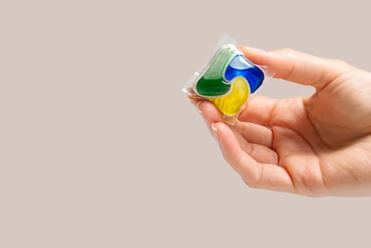 hand holds the Dishwasher Capsule on beige background. copy space, woman hand holding dishwasher detergent tablet.