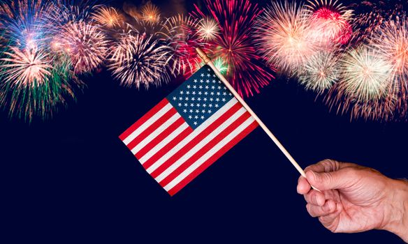 Senior mans hand holding a small toy USA flag and cutout against fireworks background